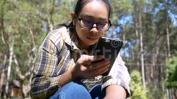 一个阳光明媚的日子年轻的女人坐在公园里在手机上读着愉快的短信视频的预览图