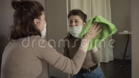 一个年轻的欧洲女孩戴着防护面具擦拭一面镜子带着防腐剂坐在家里检疫冠状病毒视频的预览图