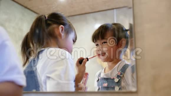 可爱的兄弟姐妹女孩化妆并在房间的镜子上一起涂口红视频的预览图