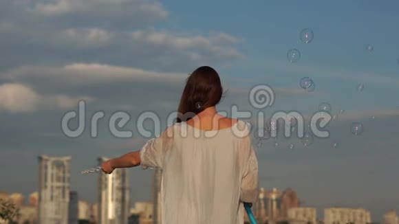 一个年轻的女孩挥动她的手在城市的背景上吹肥皂泡视频的预览图
