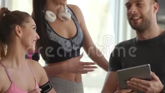 年轻女性与健身教练讨论数码平板电脑的健身进展视频的预览图