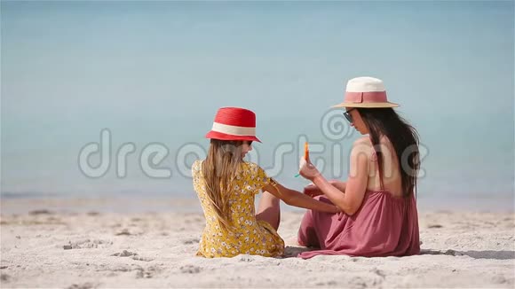 年轻的母亲在海滩上给女儿的鼻子涂上防晒霜太阳保护视频的预览图