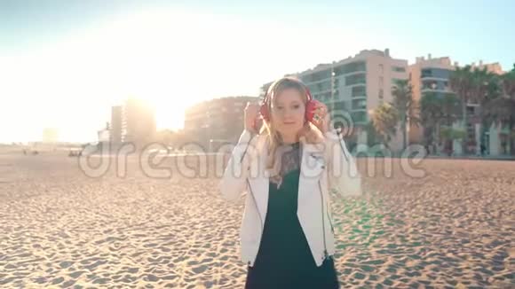 日落时分女人带着耳机沿着美丽的海滩散步视频的预览图