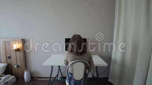 一个女孩坐在桌子前在电脑上工作的后视图特写视频的预览图