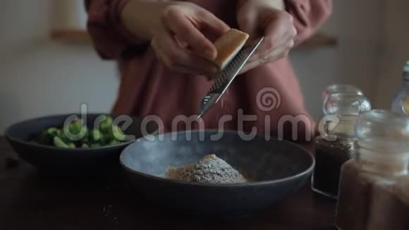 女孩在一个碗里用香料在一个小烤架上摩擦坚硬的奶酪来煮西兰花特写视频的预览图