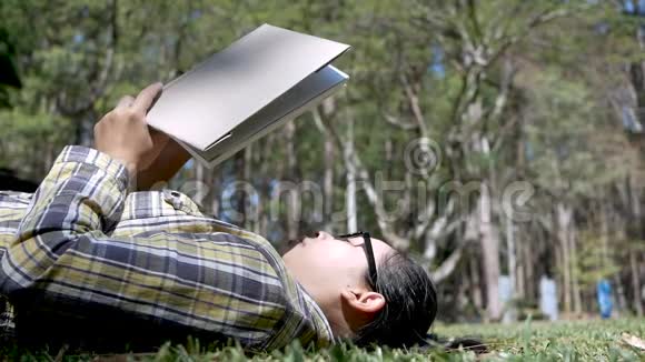 年轻的亚洲女人在度假日在花园里躺在草地上放松和阅读一本书视频的预览图