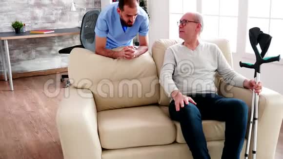 退休男子在舒适的养老院里与男性照顾者交谈视频的预览图