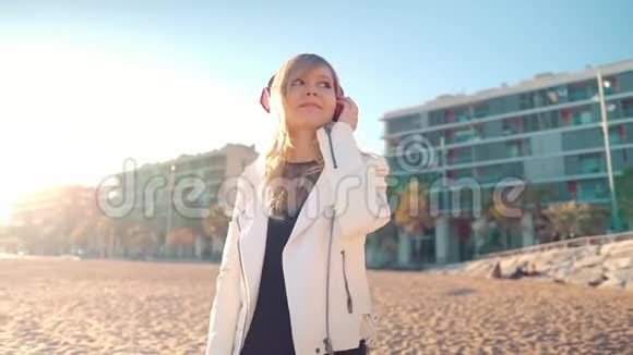 日落时分女人带着耳机沿着美丽的海滩散步视频的预览图