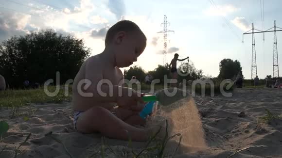 靠近电力线的城市海滩小男孩坐着玩水桶和铲子视频的预览图