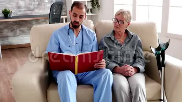 退休家庭的男护士在读一本给老年妇女的书视频的预览图