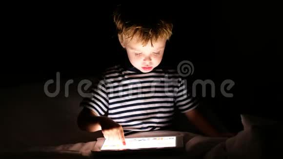 好奇的男孩在黑暗的卧室里用数码平板电脑视频的预览图