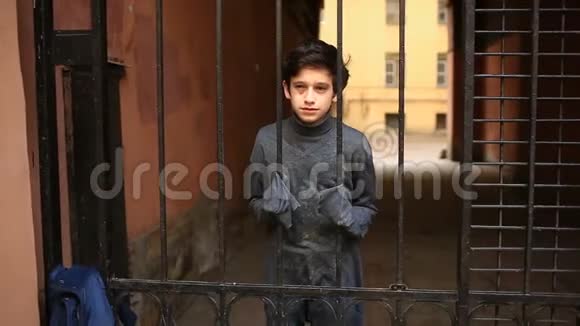 一个无家可归的少年透过铁栅栏看着摄像机视频的预览图