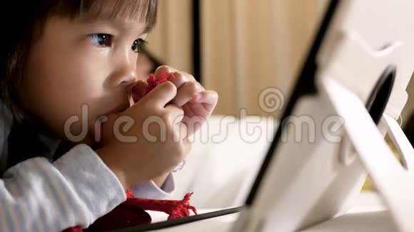 可爱的小女孩躺在床上吮吸她的拇指看着卧室里的数字平板电脑视频的预览图