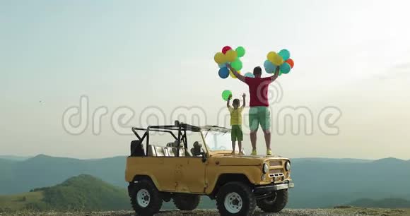 一个男人和一个男孩站在黄色的汽车上让气球飘向空中视频的预览图