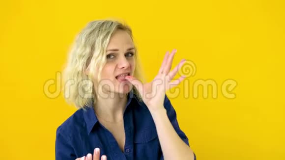 疯狂开朗的金发女孩舔手指后美味的饮食隔离在黄色的工作室背景糖果4k个镜头视频的预览图