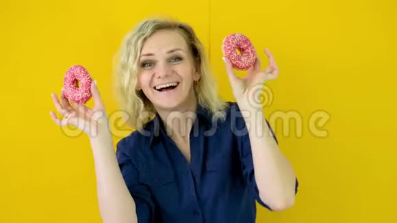 疯狂开朗的金发女孩微笑着玩得很开心眼睛上看着两个红色甜甜圈糖果黄色工作室视频的预览图