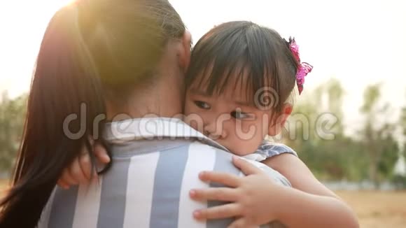 亚洲母亲在夏天的公园拥抱她的女儿小孩子在田里跌倒时哭了概念视频的预览图
