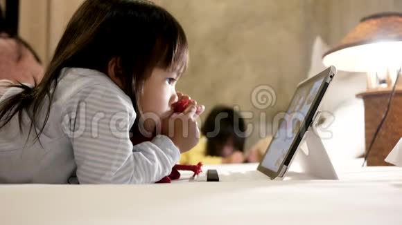 可爱的小女孩躺在床上吮吸她的拇指看着卧室里的数字平板电脑视频的预览图