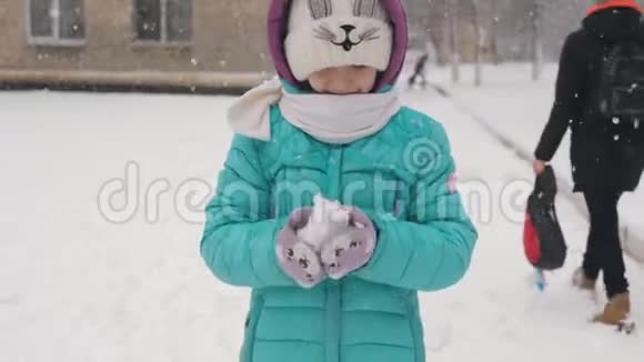 小女孩冬天从学校走回家在他手里雕刻一个雪球视频的预览图