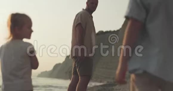 一位父亲和两个孩子在鹅卵石海滩上嬉戏玩耍的后景视频的预览图