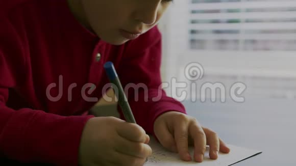 一个穿着红色毛衣的小男孩坐在桌子旁手里拿着一支钢笔在空白的白色上写字或画画视频的预览图