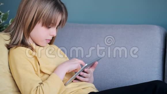 小女孩在家里坐在沙发上用她的数字平板电脑视频的预览图