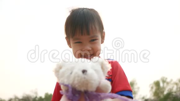 可爱的亚洲小女孩拥抱泰迪熊与感觉爱在公共公园视频的预览图