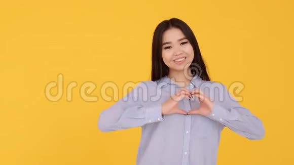 亚洲女孩表现出爱的象征用双手在黄色背景下显示心脏视频的预览图