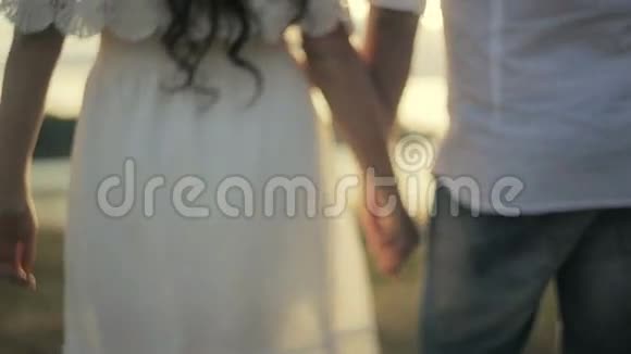 美丽的黑发女孩穿着白色的裙子强壮的年轻人穿着白色的衬衫手牵着手走向视频的预览图