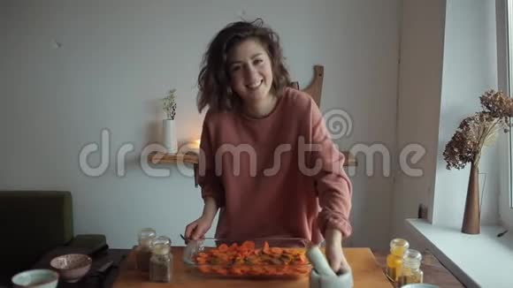 厨房里年轻漂亮的女孩把香料放在灰泥里磨碎然后在盘子里撒上胡萝卜来烤视频的预览图