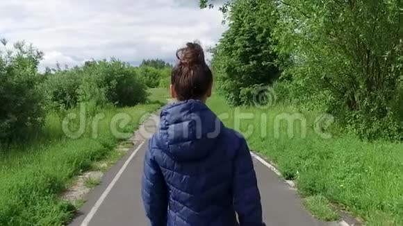 穿着蓝色夹克的年轻女子走在夏天公园的小路上视频的预览图