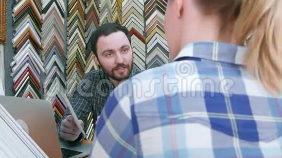 年轻人和顾客聊天谈论相框的细节使用笔记本电脑在柜台上的atelie视频的预览图