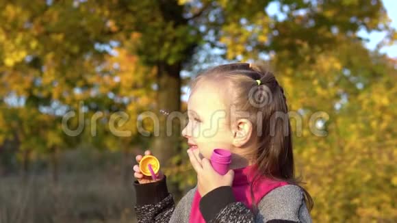 秋天公园里美丽的小女孩吹肥皂泡看着相机微笑在玩视频的预览图