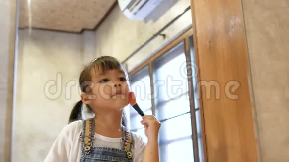 可爱的小女孩化妆并在房间里的一面镜子上有趣地刷牙视频的预览图