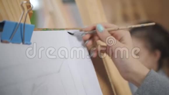 漂亮的年轻女孩在画架上画了一幅画手拿着画笔光明艺术工作室视频的预览图