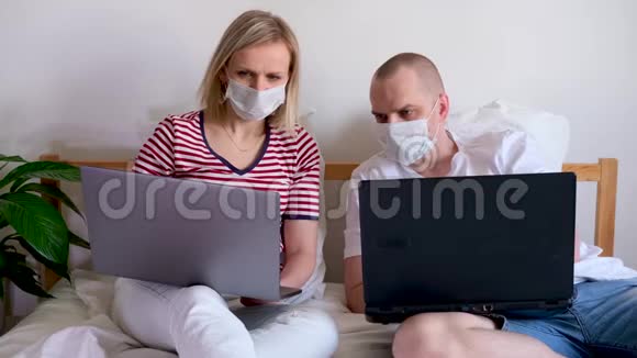 4k年轻的一家人在电脑旁的床上远程工作被隔离的夫妇冠状病毒戴着医疗面具住宿视频的预览图