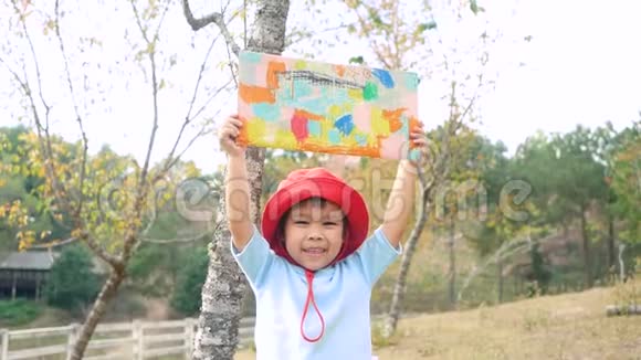 快乐的小女孩在花园里的回收纸板箱上展示她的着色工作视频的预览图