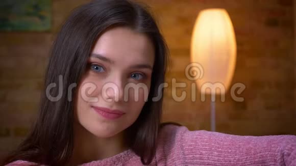 一位年轻可爱的黑发白种人白种人女孩在一个舒适的沙发上坐着看着摄像机开心地笑着特写镜头视频的预览图
