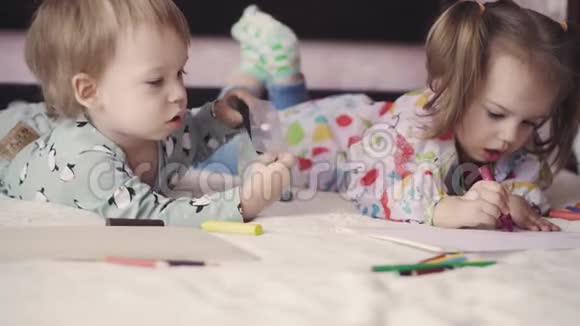 两个可爱的孩子用躺在床上的绉纱画画女孩和男孩用铅笔在床上玩兄弟姐妹双胞胎视频的预览图