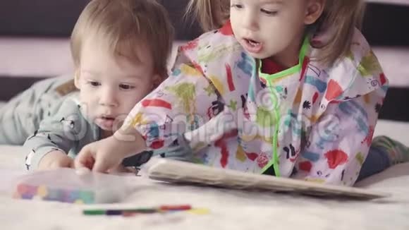 两个可爱的孩子用躺在床上的绉纱画画女孩和男孩用铅笔在床上玩兄弟姐妹双胞胎视频的预览图