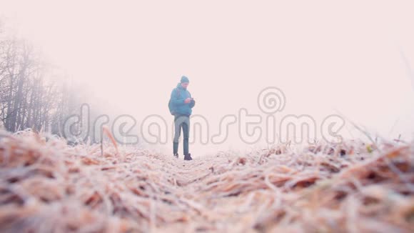 穿着冬天衣服的人站在冰冻的草地上看着智能手机屏幕视频的预览图