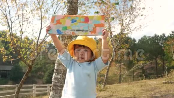 快乐的小女孩在花园里的回收纸板箱上展示她的着色工作视频的预览图