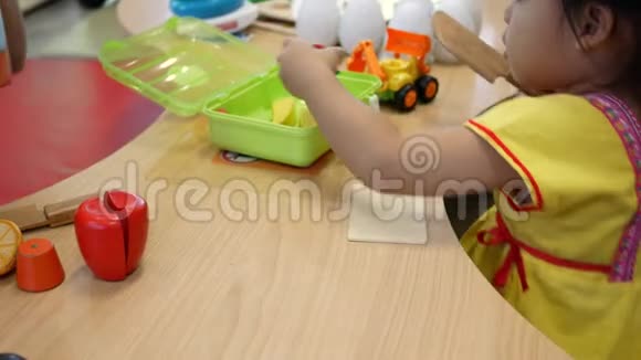 可爱的小女孩在教室的客厅玩烹饪玩具小孩用木头玩具刀切植物视频的预览图
