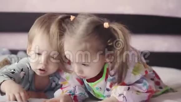 两个可爱的孩子躺在床上用蜡笔画画女孩和男孩在床上玩铅笔兄妹双胞胎视频的预览图