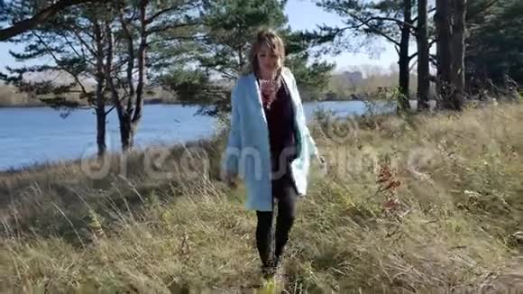 一位穿着蓝色外套的美丽年轻女子在风和日丽的秋天森林中漫步视频的预览图