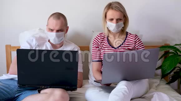 4k年轻的一家人在电脑旁的床上远程工作被隔离的夫妇冠状病毒戴着医疗面具住宿视频的预览图