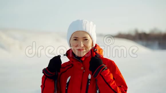 一个穿着红色夹克和白色帽子的女人看着相机冬日阳光明媚概念寒假家庭视频的预览图
