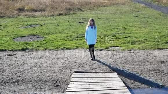 秋天穿着蓝色外套的年轻女子在湖上过桥视频的预览图