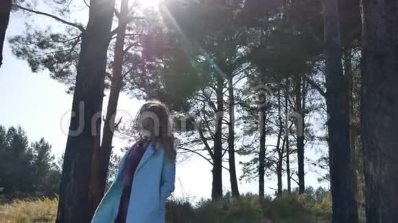 美丽的年轻女子穿着蓝色外套站在森林里风和日丽的秋天视频的预览图
