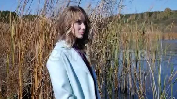 秋天湖上穿着蓝色外套享受大自然和新鲜空气的年轻女子视频的预览图